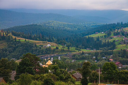 Picturesque mountain landscape. Ukrainian Carpathians. A cozy village lies in the valley below, surrounded by rolling green hills and misty mountain peaks. Bright traditional houses and untouched