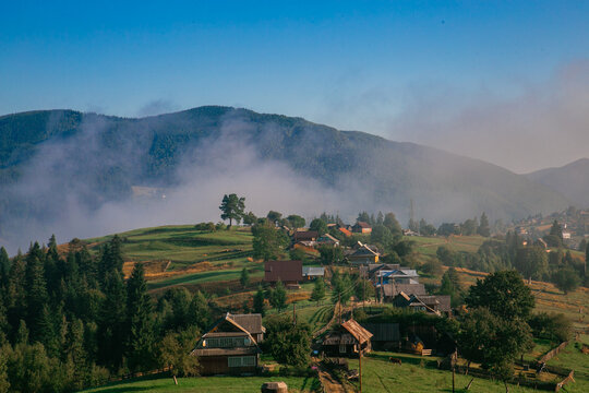 Picturesque mountain landscape. Ukrainian Carpathians. A cozy village lies in the valley below, surrounded by rolling green hills and misty mountain peaks. Bright traditional houses and untouched