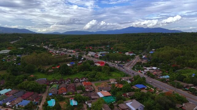 Cinematic aerial side view of a tropical village highway and distant mountains Scenic drone footage showing a rural community and lush greenery in a mountain valley landscape under a dramatic sky