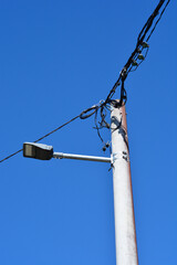 Obraz premium A vertical view of a concrete utility pole featuring a modern street lamp and a mess of electrical wires under a clear blue sky