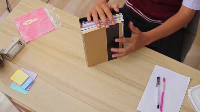 Top view of student arranging stack of notebooks and leather planner on wooden desk