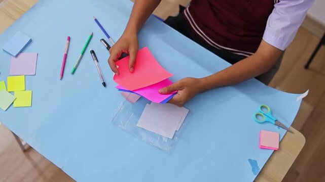 High angle shot of student organizing colorful square paper sheets for diy crafts or study