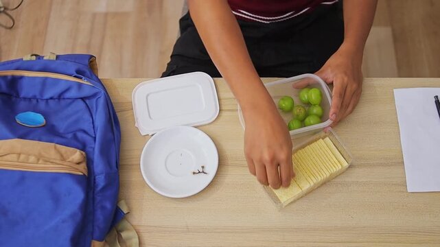 Overhead shot of student packing cheese crackers into lunch box alongside green grapes