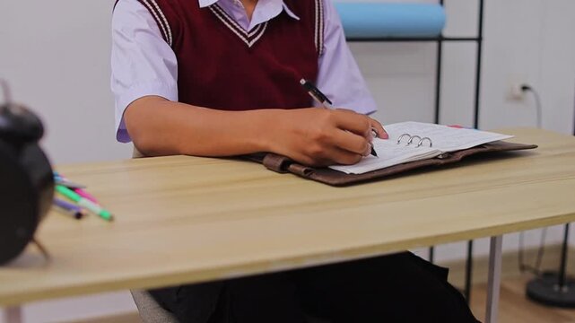 Close-up of student writing in leather journal with black pen at organized desk setup
