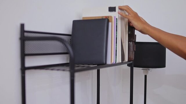 Close-up of hands student taking notebook from metal bookshelf in minimalist room
