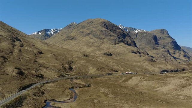Static drone shot of traffic flowing through Glencoe in the Scottish Highlands. Shot in April with snow still visible on the high level peaks. The road is the A82 from Tyndrum to Fort William.