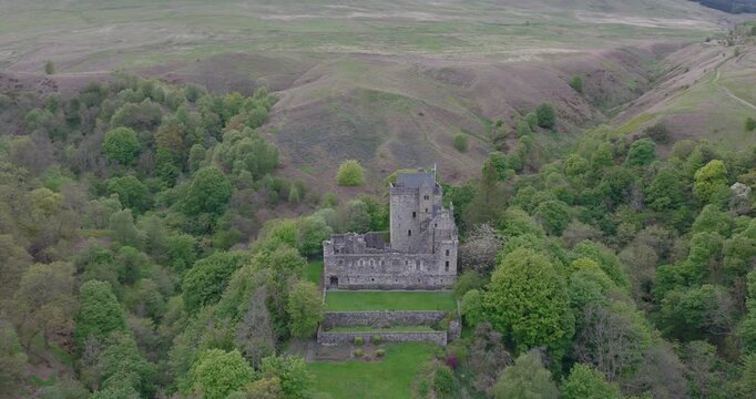 Cinematic aerial drone footage of Castle Campbell, a historic castle nestled in the Ochil Hills above the village of Dollar in central Scotland. Flyover showing the castle surrounded by lush woodland.