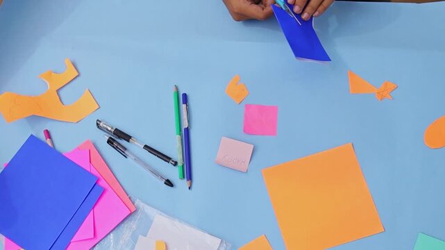 Close-up of hands engaged in creative DIY project cutting and folding colorful paper on workspace