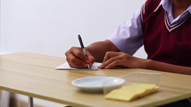 Close-up of student hands writing on sheet of paper during study session with school snacks