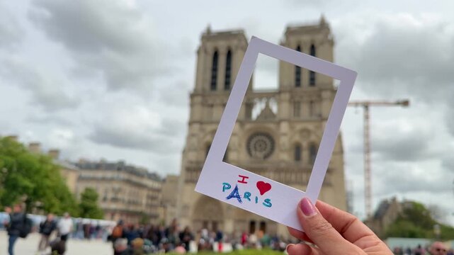 Female tourist holding a paper frame with the message 'I love Paris' in front of the famous Notre Dame Cathedral, a concept of travel, tourism, and enjoying a European vacation destination