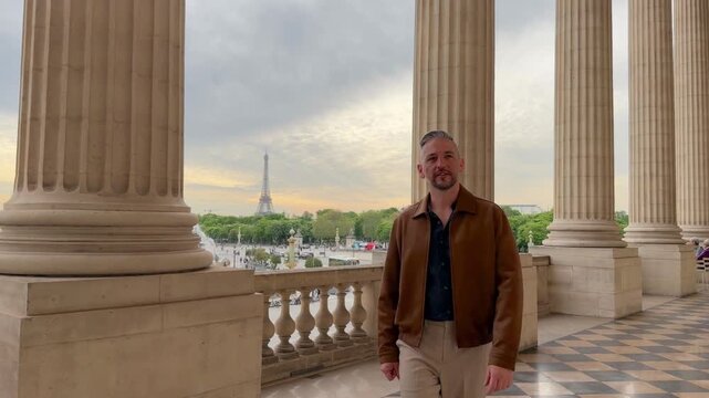 Stylish man enjoying his vacation in Paris, walking along a classic colonnade with a magnificent view of the Eiffel Tower and the Place de la Concorde in the background on a cloudy day