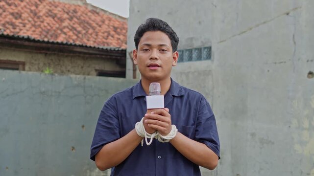 Male news reporter with hands tied rope holding microphone for representing silencing of press