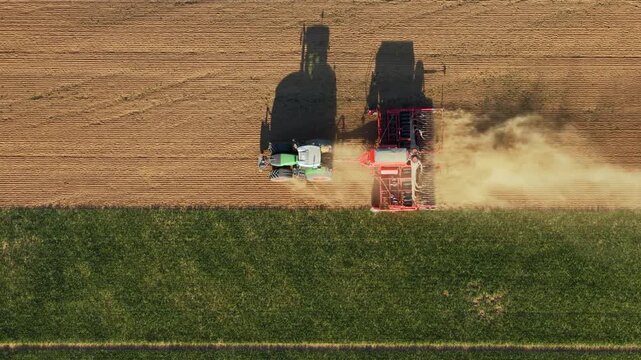 Aerial view of a tractor pulling a red seeder across a field with dust rising and long shadows Chvalkovice, Hradec Kralove Region, Czechia.