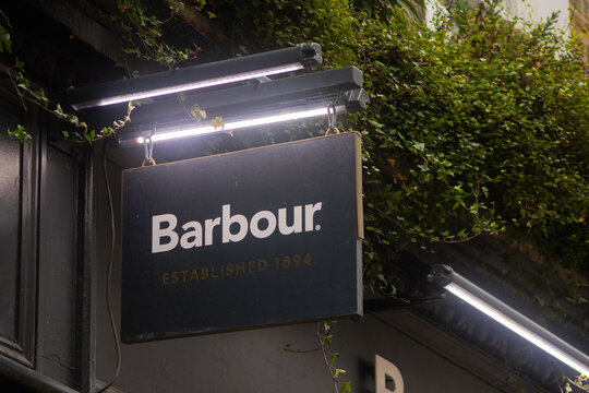 Illuminated Barbour retail store sign with ivy-covered facade at night