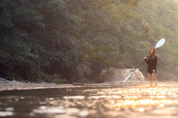 Naklejka premium Peaceful woman at river with paddle enjoying nature outdoor standing in water near forest on adventure feeling calm and confident during golden sunlight