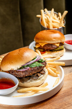Burgers and fries on plates. Two burgers are placed on white plates with fries on the side. One burger has cheese and the other has mushrooms.