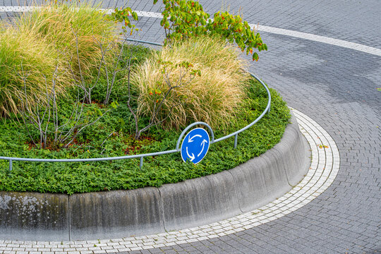 low grass and plants fill an urban island as a roundabout sign follows the pavement curve, holding the street and road edge in balance