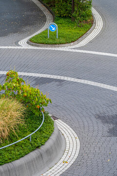a planted island with plants holds a roundabout sign beside pavement, with road marking following the street curve through an urban corner