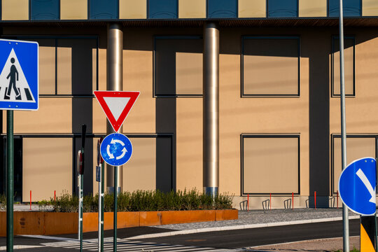an urban street sign cluster for yield, roundabout and crosswalk sits before a building facade, with columns and windows defining the edge