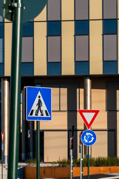 a crosswalk sign layers against building facade pattern and windows, while yield and roundabout markers hold the street beside urban columns