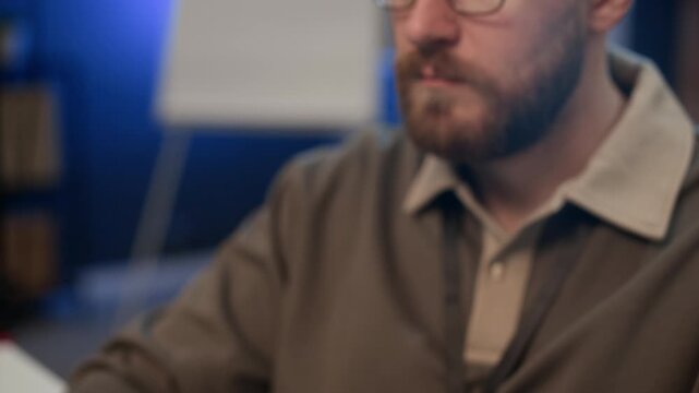 Tilt up shot of male Caucasian developer in glasses typing on keyboard of computer while working at table in modern office