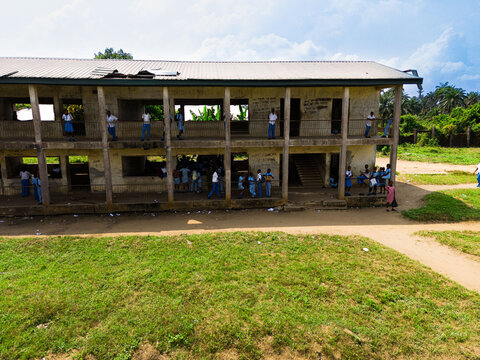 Aerial view of a two-story school building with students in blue uniforms standing on balconies overlooking a grassy field in Ahoada I, Rivers, Nigeria.