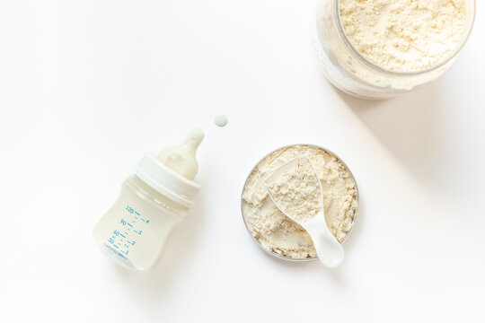 Baby milk bottle and powdered infant formula in the jar and scoop on white background. Top view.