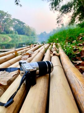 Mirrorless camera resting on a rustic bamboo raft by a peaceful river in Thailand. Concept of nature photography, travel adventure, and slow life in the tropical outdoors.