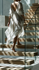 Obraz premium Woman in flowing dress walking up modern wooden stairs at home, elegant lifestyle movement in minimalist interior with copy space