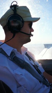 Pilot Flying Small Aircraft Cockpit with Avionics Dashboard and Clear Blue Sky Horizon. Young Male Pilot in Aviation Headset Controls Light Plane Cockpit During Daytime Flight