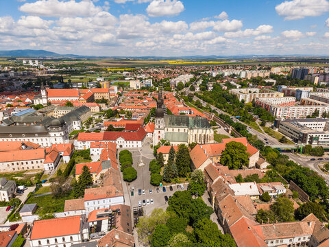 Aerial view of Saint Nicolas Basilica and the historic old town with red rooftops and green trees under a cloudy sky in Trnava, Trnava Region, Slovakia.
