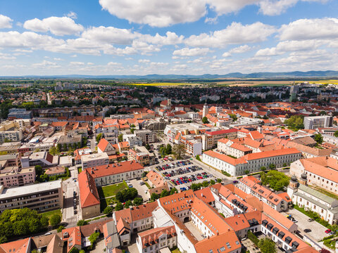 Aerial view of the historic city center with red rooftops, church spires, and a large parking lot under a blue sky with white clouds in Trnava, Trnava Region, Slovakia.