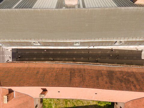 Aerial view of a narrow street between historic buildings with red-tiled and grey roofs and people walking on the pavement in Trnava, Trnava Region, Slovakia.