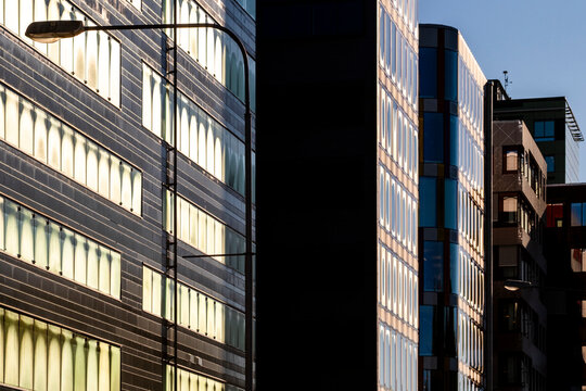 Narrow urban passage frames glass facade towers, where windows, architecture and shadow divide exterior geometry under blue sky