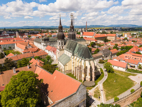 Aerial view of St. Nicholas Basilica with its iconic twin towers and the historic red-tiled rooftops of the old town under a cloudy sky in Trnava, Trnava Region, Slovakia.