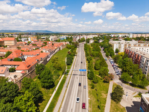 Aerial view of the historic city center with red rooftops, modern residential buildings, and a main road under a cloudy blue sky Trnava, Trnava Region, Slovakia.