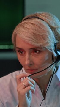 Vertical chest up shot of adult female Caucasian support coordinator reporting data via headset while working in cybersecurity office