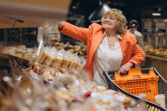 Senior woman smiling and reaching for bread from bakery shelf while shopping in a bright supermarket aisle