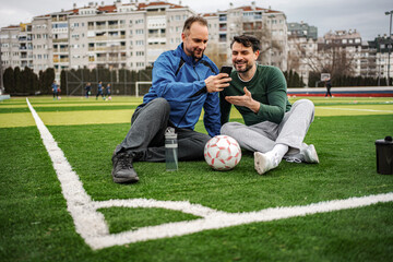 Two men relaxing on soccer field scrolling phone © Jelena