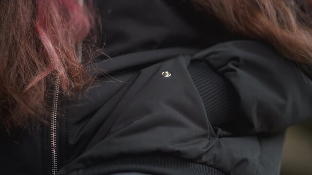 Young person adjusts sleeve during rain outdoors. Student in city adjusting jacket sleeve under rainy sky. Young individual makes sleeve adjustments on their jacket while standing in rainy city street