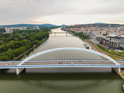 Aerial view of the Apollo Bridge spanning the Danube River with the city skyline and Bratislava Castle in the distance under a cloudy sky in Bratislava, Bratislava Region, Slovakia.