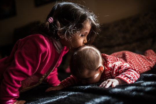 ittle Girl Kissing Baby Sibling in Warm Sunlight at Home