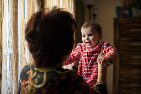 Grandmother Holding Happy Baby Near Window in Cozy Home