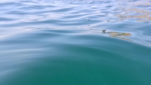 Sea Water Surface gentle ripples move across calm turquoise ocean water near a coastal cliff on a peaceful summer day