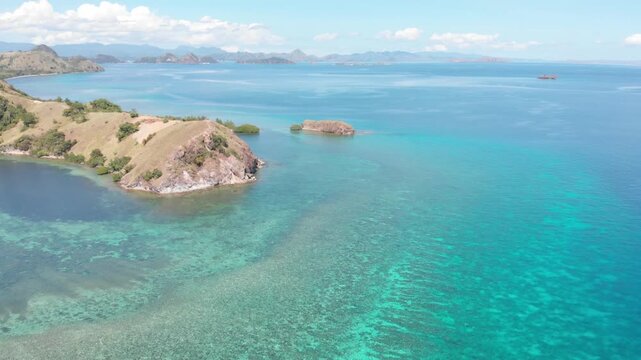 Aerial view of the northern headland near Labuan Bajo in Komodo National Park, Indonesia, surrounded by vibrant coral reefs and turquoise tropical waters under a sunny blue sky
