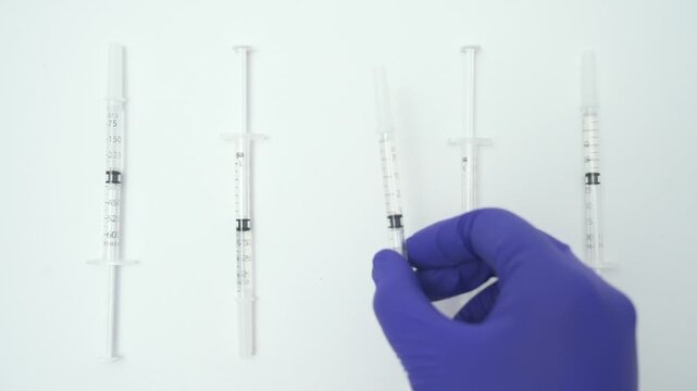 Doctor's hand in a blue latex glove taking a single syringe from a row isolated on a white background