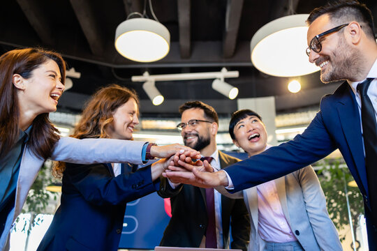 Diverse business team stacking hands, smiling and celebrating success, concept of collaboration and partnership in office