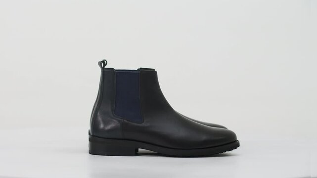 Pair of classic black leather men's Chelsea boots spinning. Stylish and modern footwear isolated on a clean white background