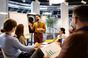 Business professional leading meeting presentation on whiteboard, sharing ideas with diverse team in modern office