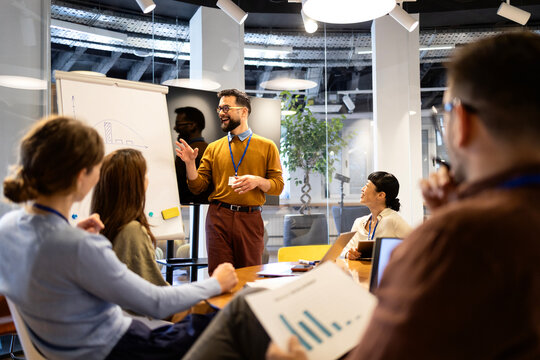 Business professional leading meeting presentation on whiteboard, sharing ideas with diverse team in modern office